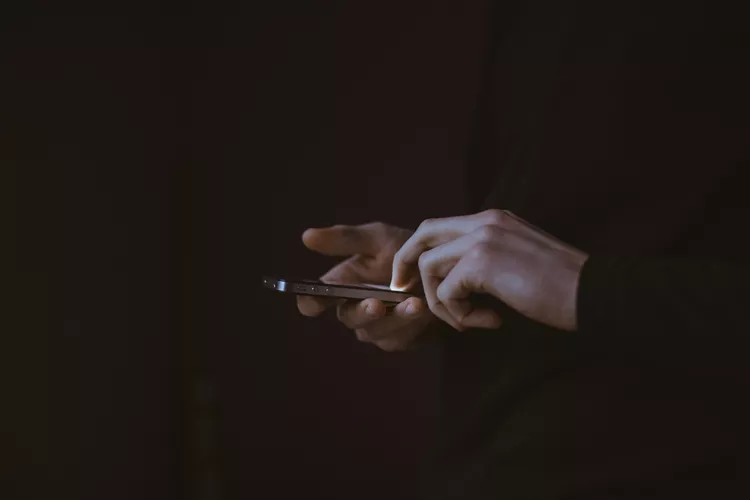 Hands using a phone on a black background. Gilles Lambert